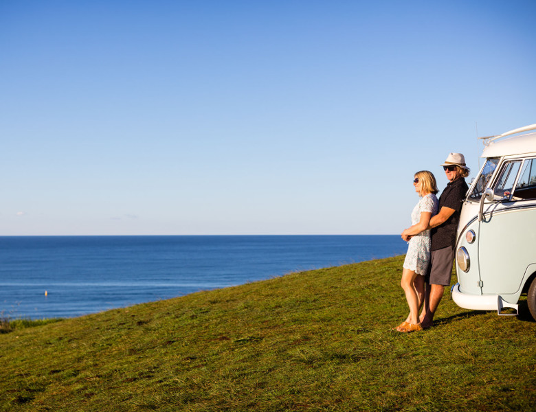 Couple leaning on Kombi overlooking beach