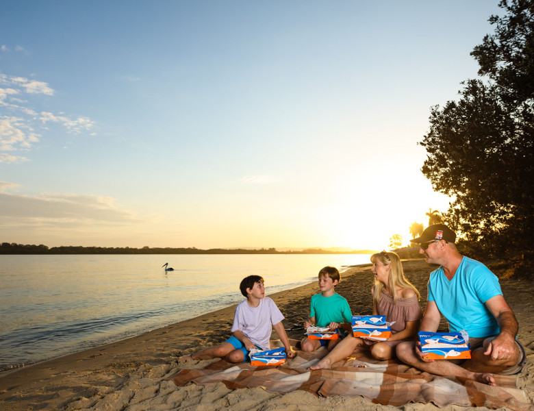 Family eating fishing and chips on river at sunset